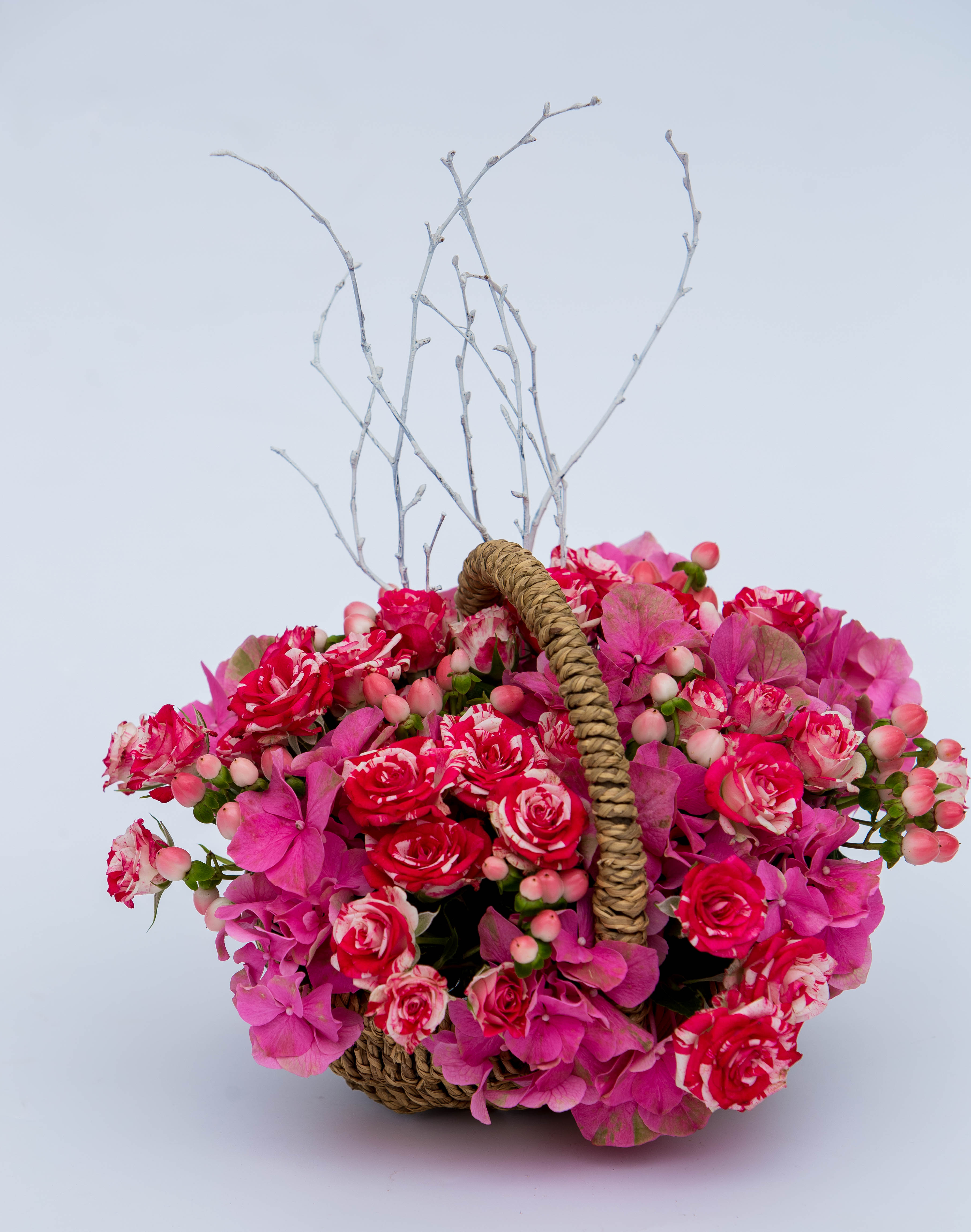 Shades of pink hydrangeas and sprayed roses in a medium cane basket